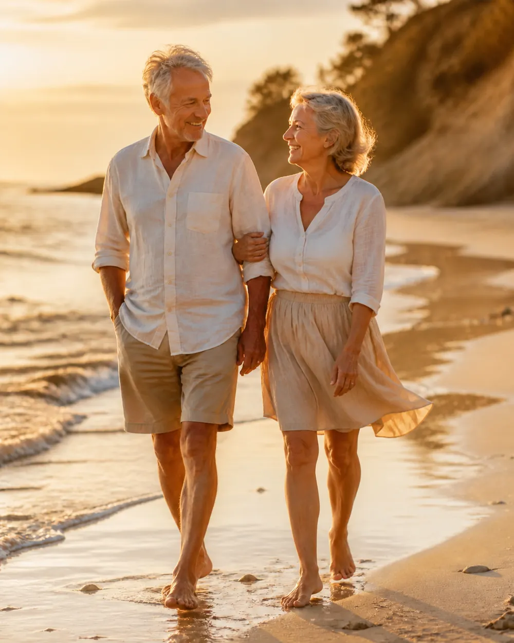 Casal de idosos caminhando na praia, ele de shorts e ela de saia, com pernas saudáveis